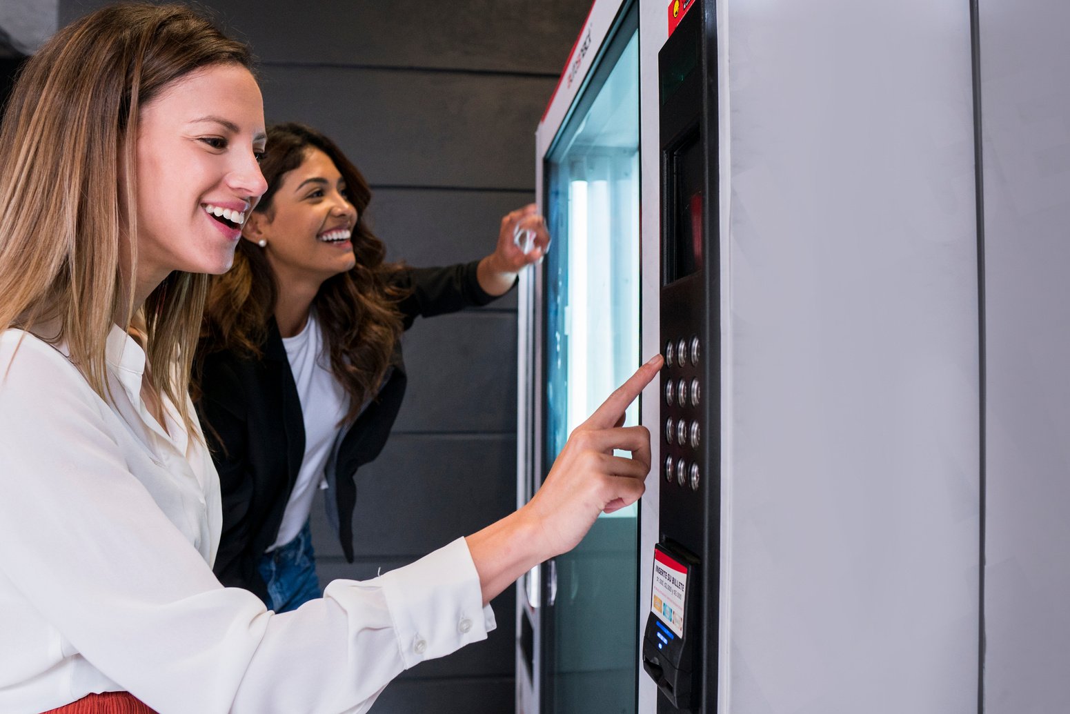 Female coworkers taking food out of vending machine